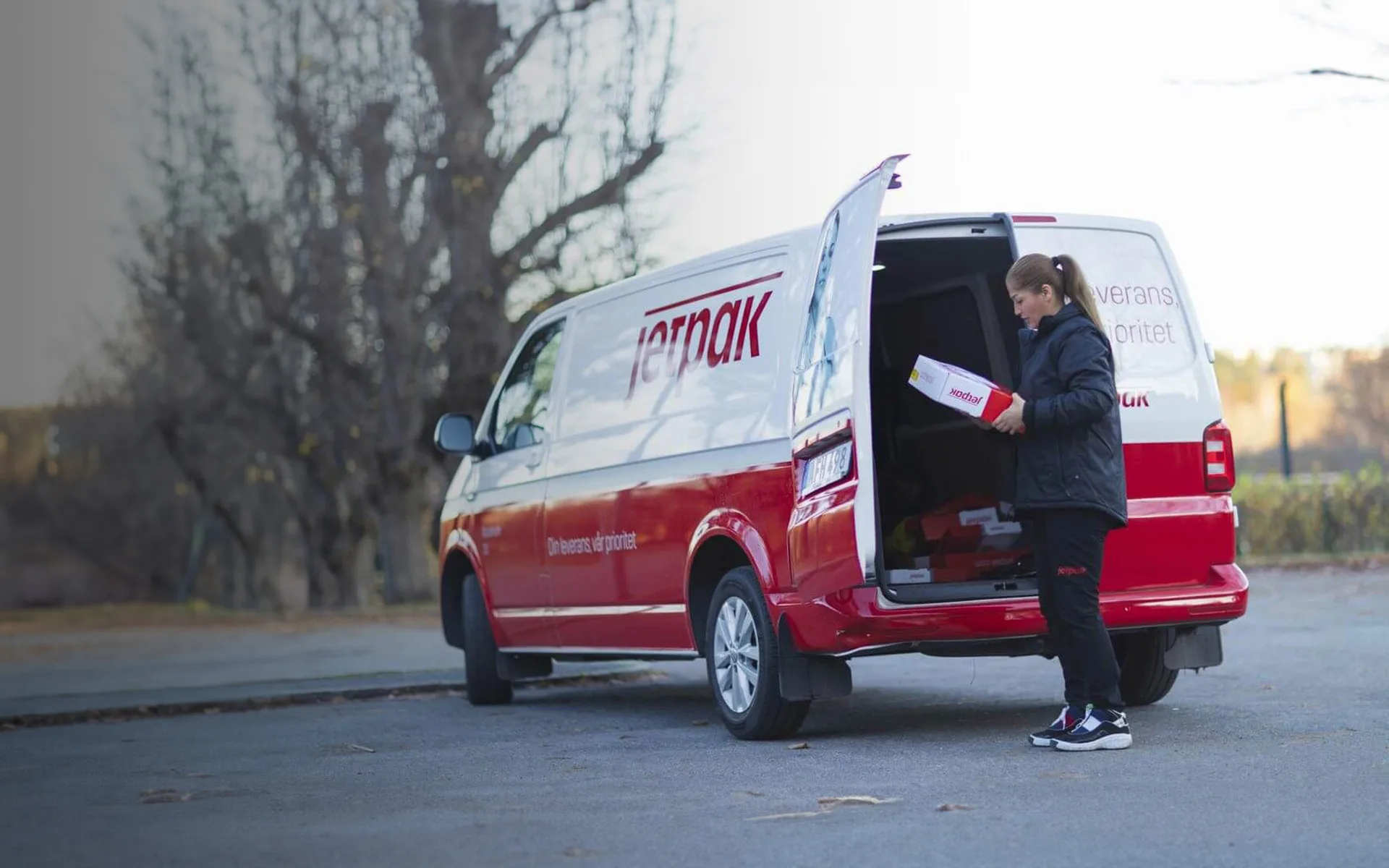Jetpak-bil med kvinna som plockar fram ett paket från bakluckan.